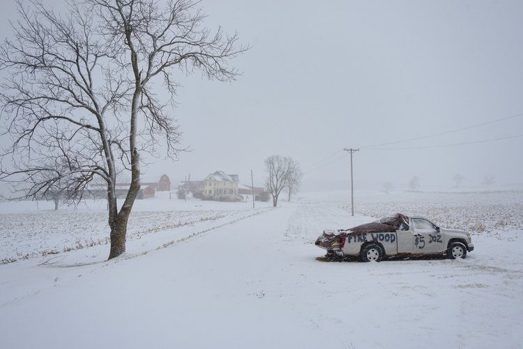 Photo of a snowy Wisconsin field with a run down truck with text reading "Fire Wood $5 A Dozen" and a farm house in the background by Paul Yurkovich.